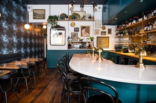 The original oak floors were restored to reveal the patina. White oak shelving, made by local outfit Jewell Hardwoods, displays the wine selection and an assortment of art. The custom pendant lights above the tables are by local designer Nash Martinez of Current Collection.