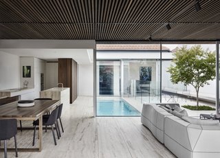 For the finish palette, the architects have chosen travertine and timber, using the wood strategically to foster flow. Travertine lines the floor, counters, and kitchen island, while timber is used to define the ceiling, highlight feature walls, and encase cabinetry.