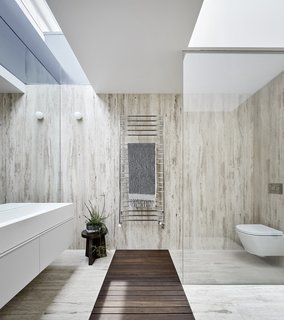 In the bathroom, skylights have been placed in the existing roofline to bring in more natural light. A glass partition and frameless mirror visually expand the space.