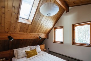 The cabin has three bedrooms. The main bedroom was brightened up with a new coat of white paint and is furnished with Schoolhouse Electric sconces, the Nelson Bubble Lamp from Design Within Reach, and linens from CB2.