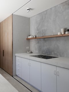 In the kitchen, white concrete counters top white cabinetry and abut a tile accent wall. The streamlined palette of the house "originated from a desire to have a space to unwind in that wasn't over-saturated with trends or design features or glossy plastic finishes," say the architects.