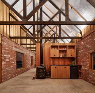 Salvaged brick was left unfinished on the interior, without a "sheet of plasterboard in sight," the architects continue to explain. Reflective roof insulation at the ceiling redistributes the light from concealed LED fixtures at the timber trusses.