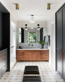 In the master bathroom, the Clé Tile floor, custom walnut vanity, and marble counter fashion a luxe retreat. Lighting is from a mix of manufacturers, including One Forty Three, Rejuvenation, Cedar & Moss, and Atelier de Troupe. The faucet is from Watermark.