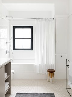 The white subway tile on the tub surround and cream penny rounds on the floor (both from Nemo Tile) create textural contrast in the same color palette. The stool is from Serena & Lily.