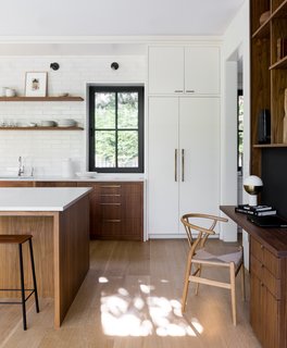 A modern desk was incorporated into the built-in walnut unit that separates the kitchen from the dining room, and has been accented with a Hans J. Wegner Wishbone Chair. The refrigerator and freezer columns are Thermador and the wall sconces are by Cedar & Moss.