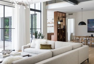 An L-shaped living, dining, and kitchen area overlook the backyard via full-height, triple-paned units from European Architectural Supply. "These high-performing European windows have substantial frames that are designed to not conduct cold and are also very well-sealed," the architects add. They used Schuco AWS75 Aluminium for the large first-floor units and Schuco SI82 uPVC for the smaller second-floor units. The striking drapery is from The Shade Store.