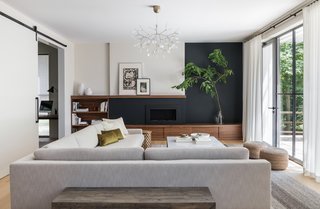 Walnut storage, both open and closed, frames a black-painted wall with a fireplace at its center. The wall treatment can also hide a future television. "A dark wall is a great way to keep a large screen from feeling like a big black hole on the wall," notes the firm.