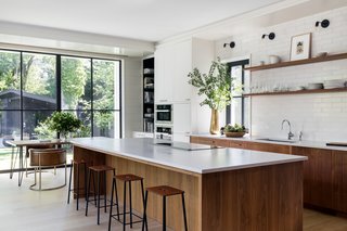 In the kitchen, White Oak floors, inset walnut cabinets, Fireclay subway tile, and Caesartone countertops read more classic vibes, while the furnishings—such as the Reno Table from Structube, Channel Chairs by Industry West, and ADAM Stools by Frama Denmark—are modern counterpoints. Appliances include a Thermador 36" Freedom Induction Cooktop and an inconspicuous Thermador 36" Downdraft Ventilation, as well as a Miele Dishwasher, convection oven, and speed oven.