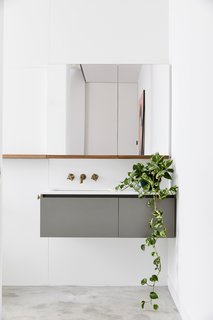 Bathroom finishes are an inversion of the darker palette in the main spaces, using a white, reconstituted stone counter atop a laminate cabinet with blackbutt shelves and brass faucets.