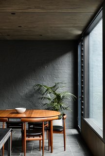 In the dining room, a vintage dining set is offset by the painted brick wall of the original house. Lowered ceilings in the eating area provide an intimate setting within the larger space.