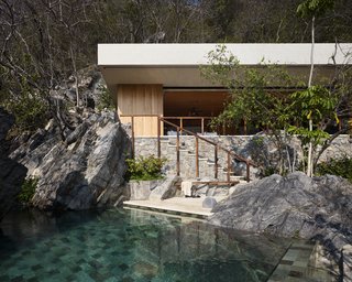 The sand-colored fascia of the roofline integrates the palapa into its environment, as does the stone wall facade, which blends in with the boulders.