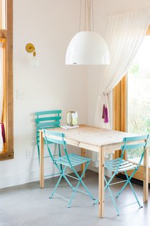 A petite dining table is surrounded by sky blue chairs that sync with the nearby kitchen cabinets. The pendant is the Factory Light No. 9 Pendant from Schoolhouse Electric.
