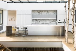 These 30 White Kitchens Are Anything But Ordinary - Photo 3 of 30 - An expansive skylight extends the full width and length of the kitchen, flooding natural light into the core of the open and connected living spaces.