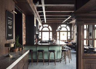 History and Modernity Meet in This Industrial Hotel and Restaurant in Philadelphia - Photo 8 of 11 - A quote bar hangs on the wall upon entry into the bar. Walnut wood tones and black furnishings are accented by the green pastel bar. 