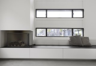 Custom benches with integrated storage and a fireplace sit below the windows lining the exterior walls of the open living space.
