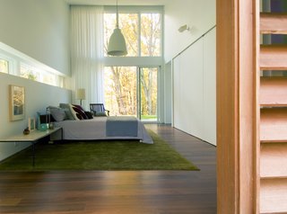 Large windows continue into the master bedroom. A green rug connects the colors of the exterior with the interior space. 