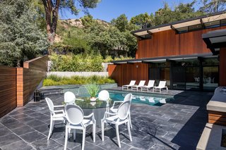 An Award-Winning Midcentury Residence in Los Angeles County Asks $3.9M - Photo 14 of 17 - The pool, accessed from the main level, is surrounded by the same dark floor finish as the interior. Bright white chairs and loungers contrast with the dark materials. 