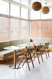 A built-in banquette with light green, tweed patterning is paired with tropical, wooden folding chairs. 