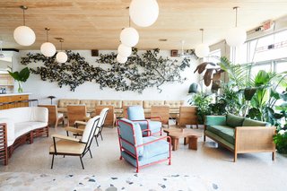 A mix of contemporary and 1950's furnishings fill the lobby bar space, accented with greenery and globe pendant lights. A floral art installation, crafted from Ralph Lauren shirts, stretches across the wall.