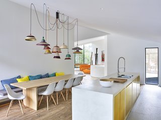 The combined kitchen and dining area is infilled with pops of color. Metallic gold cabinets and decorative pendants by Alvaro Catalan de Ocon accent the open space.