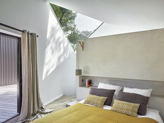 Triangular skylights also make an appearance in the master bedroom. In addition, a concrete partition wall with a recessed bookshelf provides a custom headboard solution.