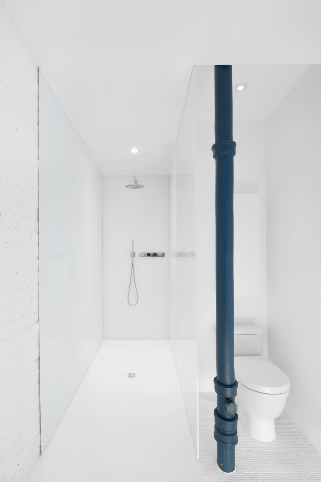 White laminated glass creates the shower surround. A blue painted pipe adds a singular color element to the bath space.