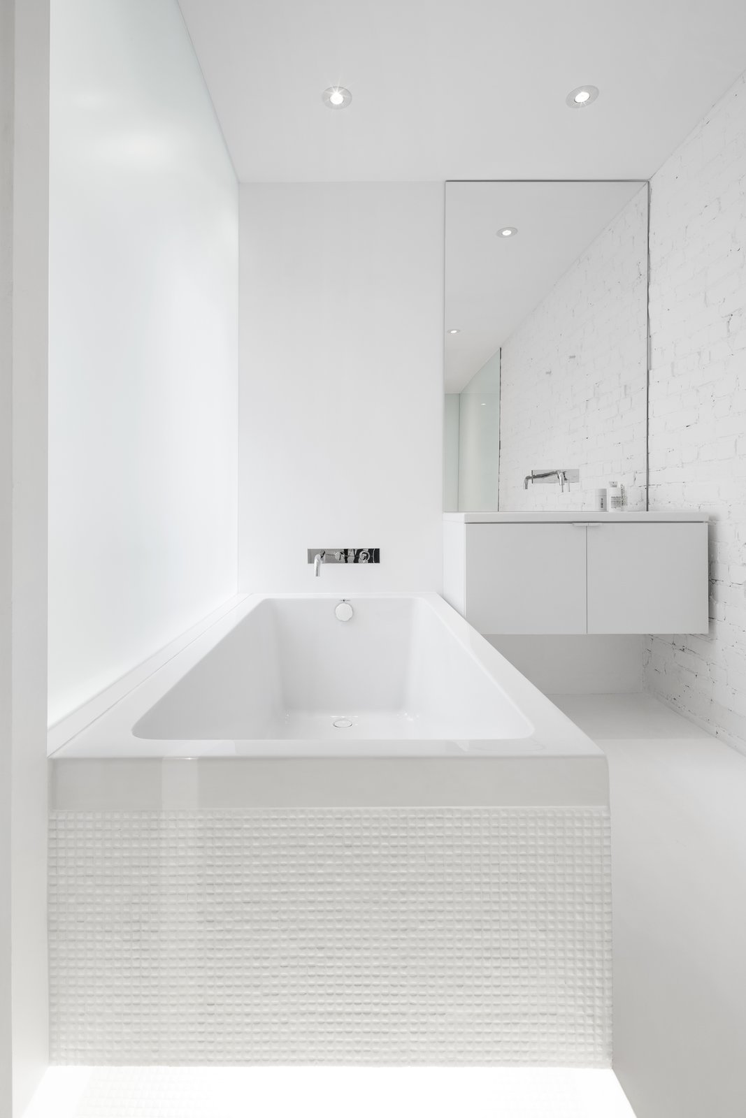 An opaque glass wall which extends the length of the tub, allows filtered light into the bath space. All white elements allow the light to reflect, creating a bright interior.
