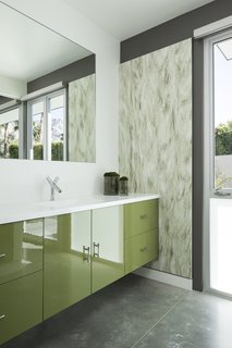 Glossy green cabinets, textured wall coverings, and polished concrete floors in desert hues decorate one of the guest baths.