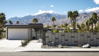 A steel-framed canopy leads directly to the front entry of the dwelling. A concrete block fence provides privacy from the surrounding neighborhood. Drought-tolerant landscaping dots the landscape.