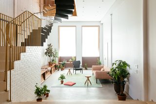 A Steel Staircase Merges Two Units Into One in Tribeca - Photo 8 of 13 - Large windows at the front of the house draw in an abundance of warm light. Custom millwork frames the windows while also providing storage in the living room. Hues of pink and green splash between furnishings, textiles, and plantings.