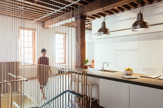 A Steel Staircase Merges Two Units Into One in Tribeca - Photo 11 of 13 - White cabinetry flanks the far wall of the kitchen. Industrial pendants hang atop the concrete topped island. Metal rods extend to the exposed wood decking above.