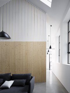 The staircase is concealed between wood paneled walls adorned with white, wooden slats, allowing light to filter in while also creating a subtle division between spaces. 