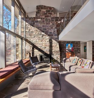 Full-height glazing allows daylight to fall deep into the home, extending into the mezzanine. A stone fireplace anchors the living space while extending upward.