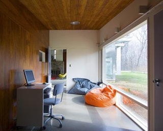 The children's playroom sits off one end of the living space, adjacent to the kitchen and children's bedroom. Full-height windows look south onto the tree-covered land.