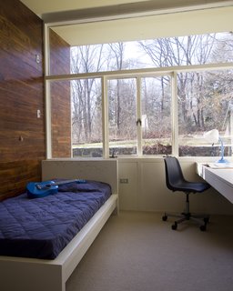 Wood siding extends from the interior of the children's bedroom to the exterior. A built-in desk sits just below the window sill. Large windows provide a direct connection to the outdoors.