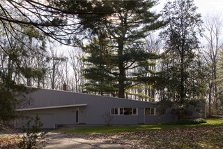 Nestled between trees, the front facade of the home is minimal with sloping roof planes, painted wood siding, and ribbon windows.