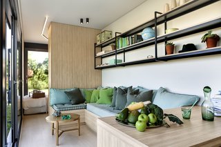 Colorful teal and green cushions decorate the built-in wood furniture. Simple open shelves extend along the living space, providing additional storage.