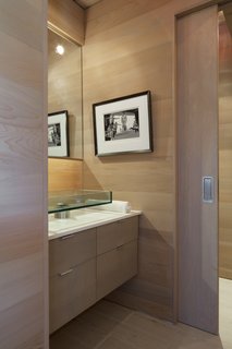 A floating wood vanity with a glass pedestal sink is a sleek solution in the main floor bath. A wood pocket door conceals the water closet.