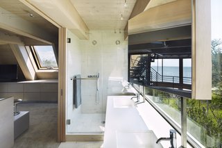 In the master bath, views do not diminish. A glass-enclosed shower and double vanity look onto the surrounding land. A post-mounted mirror provides vanity space while not blocking the views.