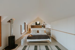 On the upper floor, the peaked roof form is revealed. A built-in headboard provides some separation between the functional spaces within the suite.