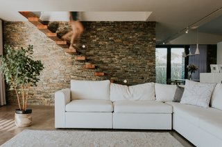 The floating wood stairs descend in front of a stone wall, which extends from the outside in.