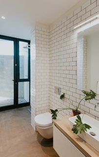 Simple subway tiles decorate the walls of the main floor bath. A seamless concrete floor leads to directly to the shower with full-height glazing.