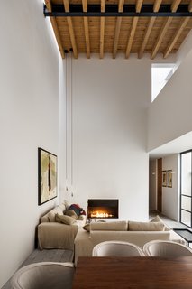 In the main living space, two sofas are arranged around a fireplace, with long pendant lights hanging from the high ceiling.