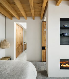 The minimal, modern character extends into the bedrooms. Simple steel shelves are embedded in the wall above a linear fireplace. A rattan pendant hangs above the nightstand.
