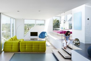 In the main living space, brightly colored furnishings—including an iconic womb chair and a sofa from Ligne Roset—create a playful interior space for lounging. A laminated glass floor allows light to pass further between the various levels.
