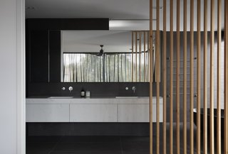 The master bath is a luxurious retreat wrapped in dark tiles and completed with a floating vanity and soaking tub. The wood slats make an appearance, somewhat resembling the flowing curtains and surrounding trees in the background. 