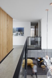 A catwalk, bordered by a modern steel-and-glass railing and a vertical wood-slat wall, connects the four bedrooms on the upper floor.