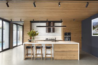 The kitchen is tucked under the living spaces above and wrapped in a warm wood finish. The use of marble as a continuous countertop and backsplash creates a clean, contemporary look.