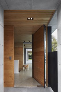 Wood accents, evident in casework, doors, and the wood-slat ceiling, provide warmth against the cool, bluestone facade. A large wood-and-steel pivot door serves as a grand entry.