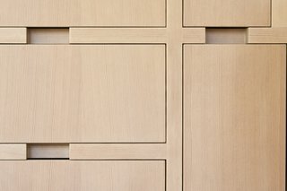 The custom wood joinery uniquely eliminates the addition of pulls through a recess in the cabinets. The whitewashed wood with a matte sealer is a sleek, modern finish that blends nicely with the wooden slats in the atrium.